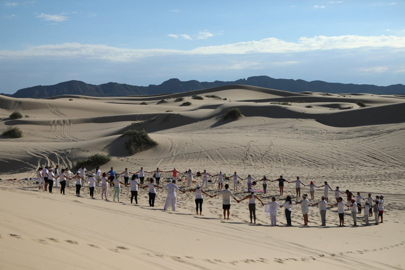 A circular gathering of yoga enthusiasts and a symbolic movement for peace during a yoga event in the dunes of Mexico