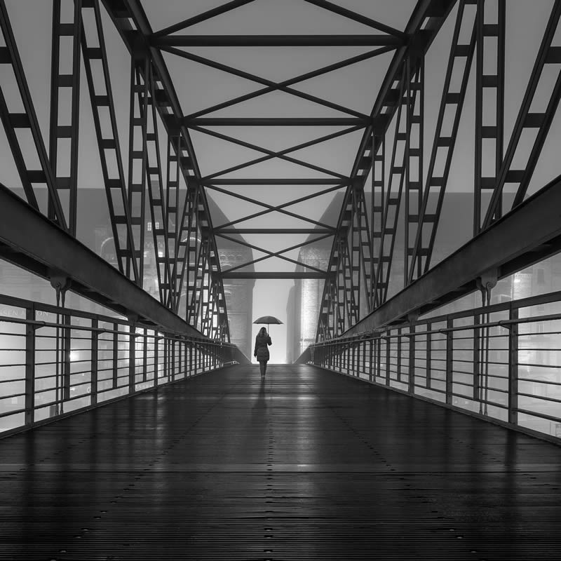 A woman crossing the bridge with an umbrella