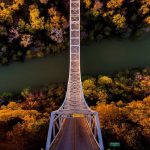 A panoramic photo of a bridge between the forest and the river