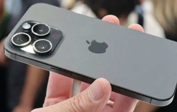 A close view of the flagship iPhone's triple camera module in the user's hand, with a matte design and Apple logo in the center of the back cover