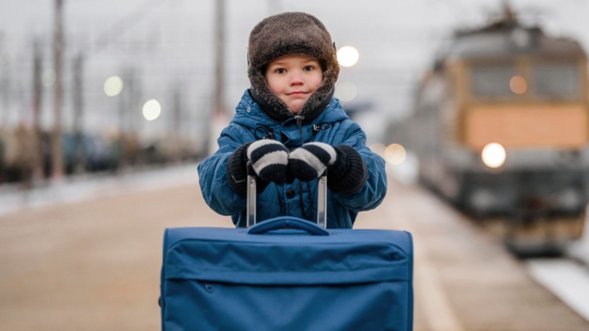 Children with winter clothing next to blue suitcase