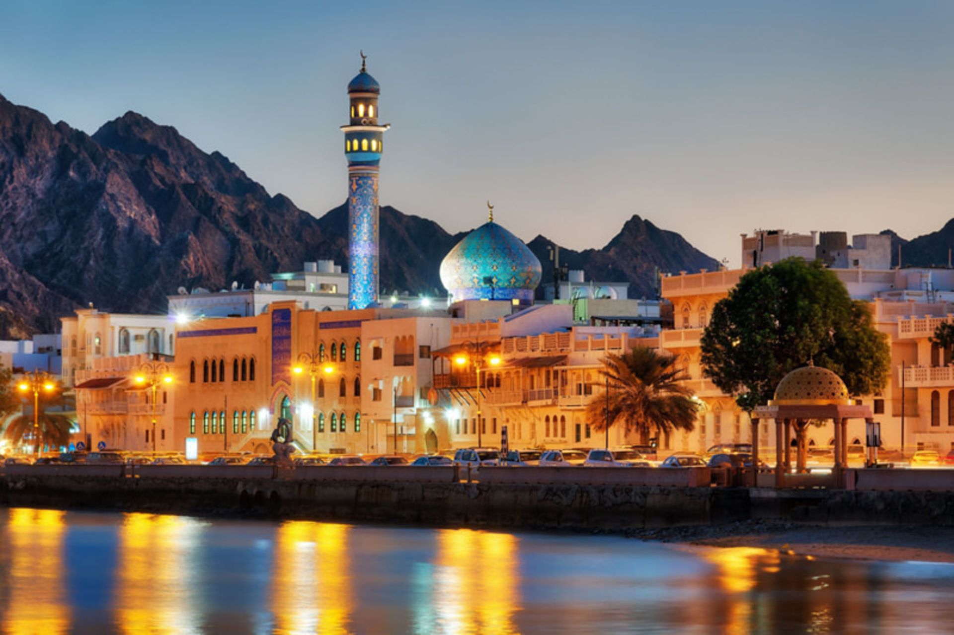 Oman Muscat City at sunset with mosque minarets, green dome and background mountains