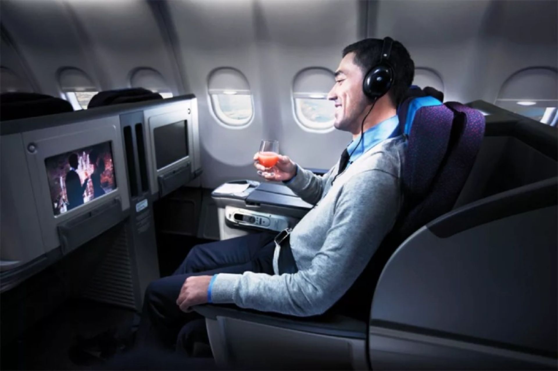 A man with headphones eating and watching movies on the plane