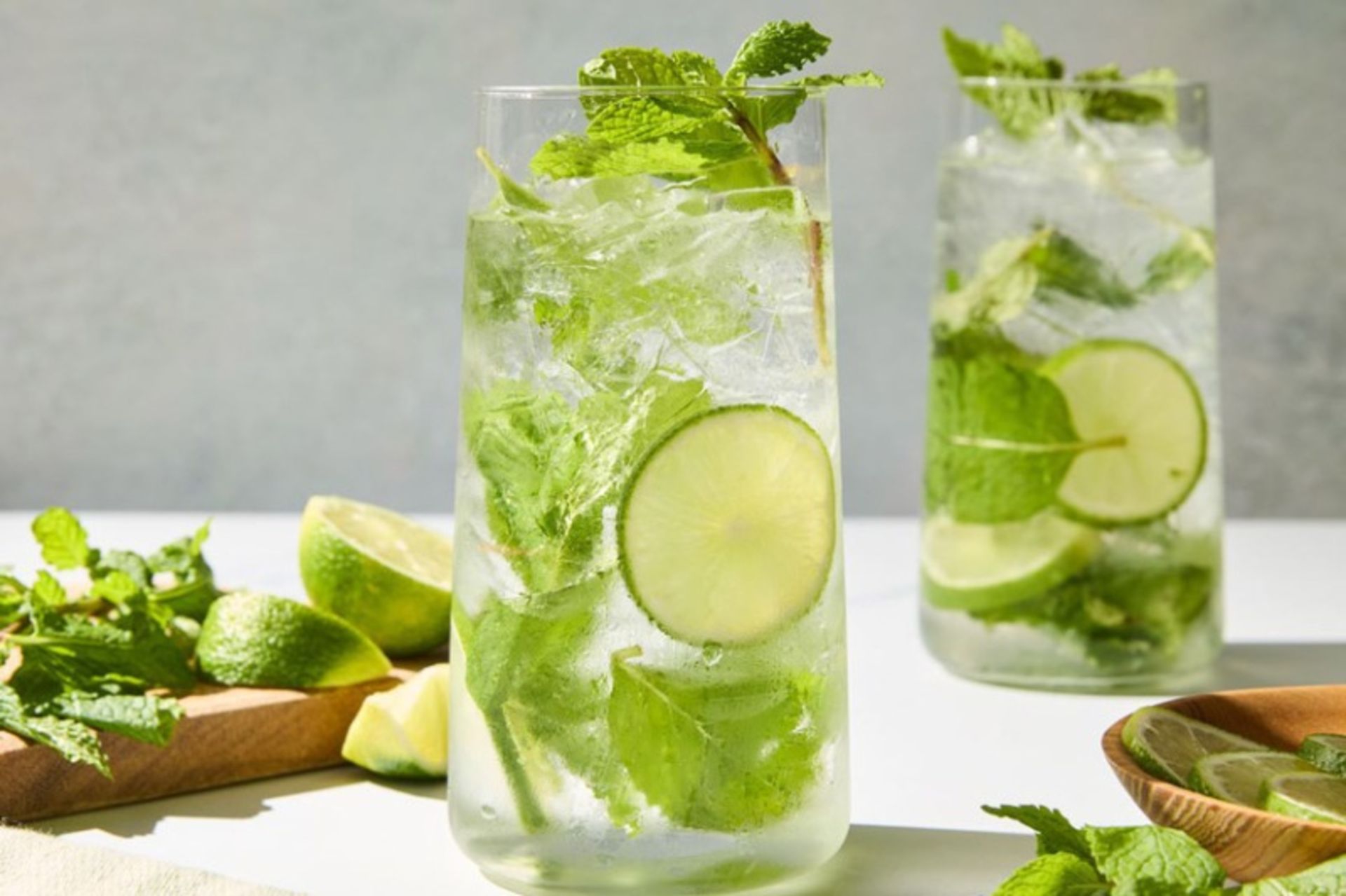 Two glasses of classic Mohito next to the mint leaf and lemons
