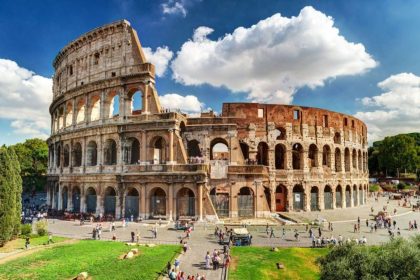 Colosseum amphitheater on sunny day, blue and cloudy sky, surrounding green space and visitors