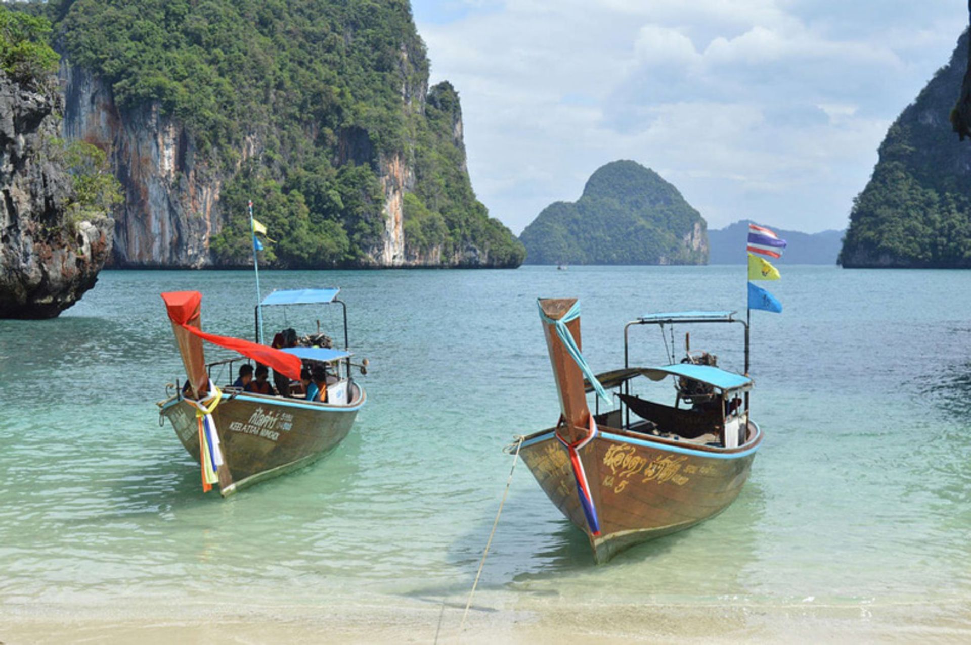 Two boats in turquoise waters and next to the lush limestone cliffs 