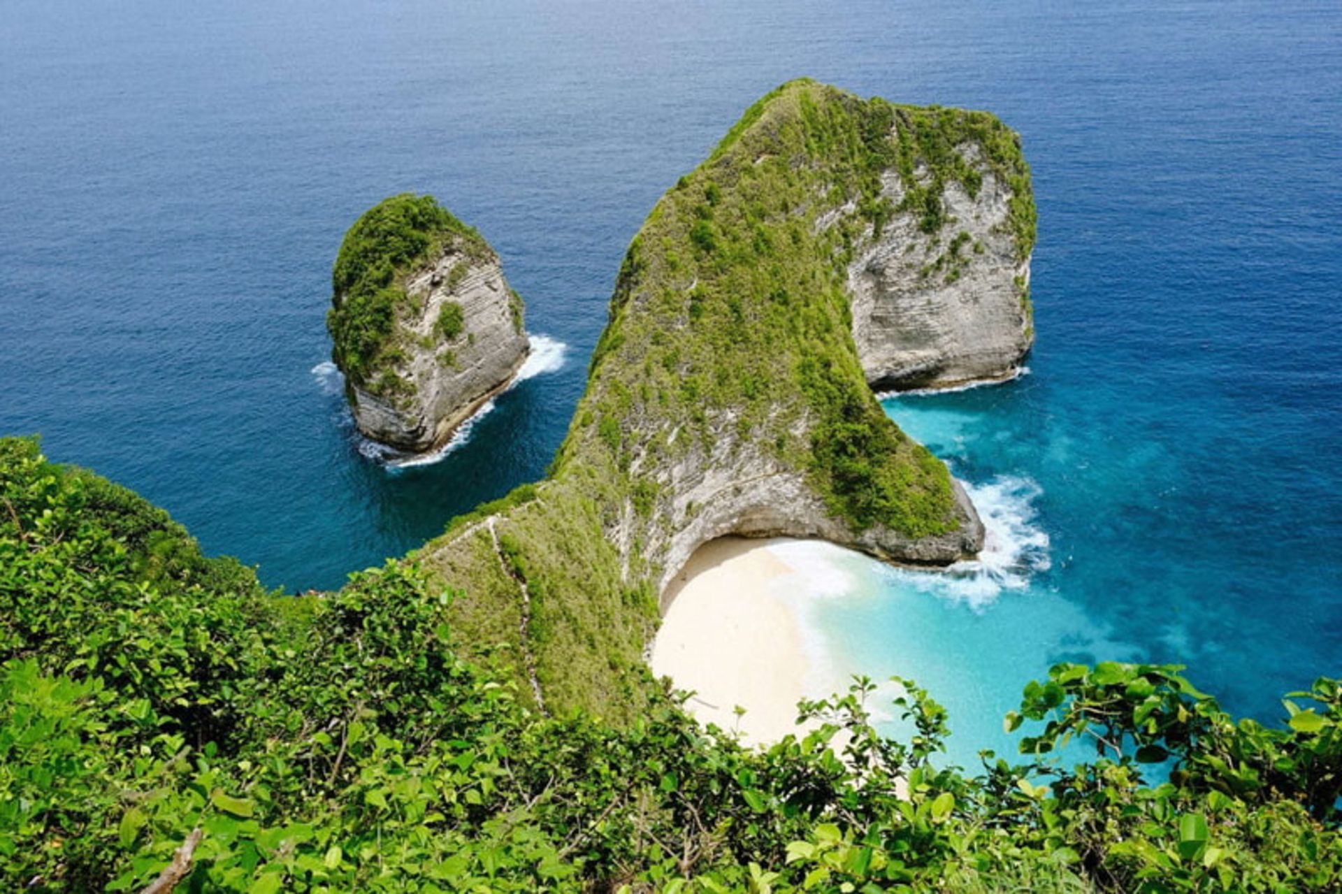 A lush rock on the white sandy beach and turquoise waters of Bali Island