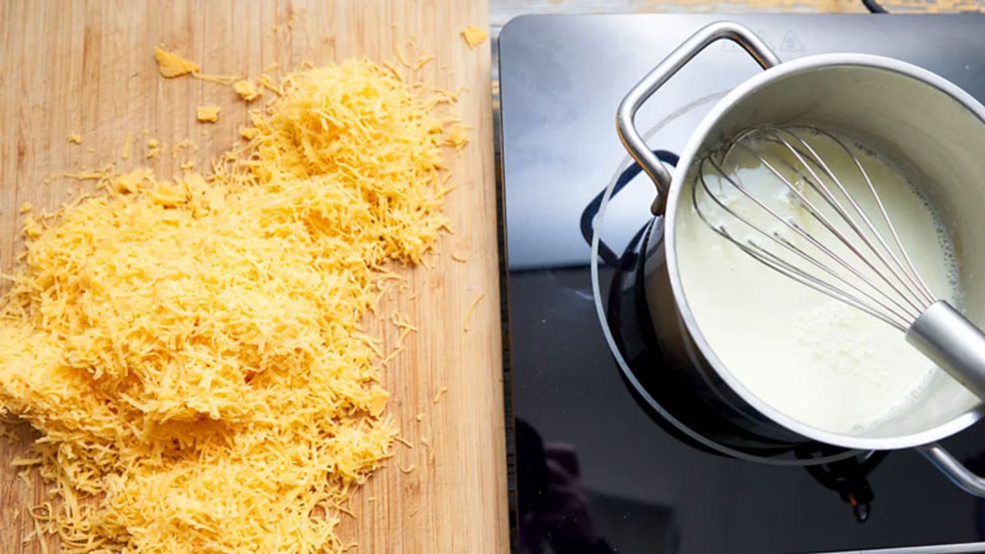 Grated cheese on a wooden board next to a pot of milk