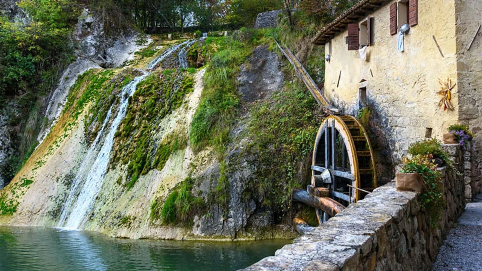 An old water mill next to a waterfall and a stone building in Treviso