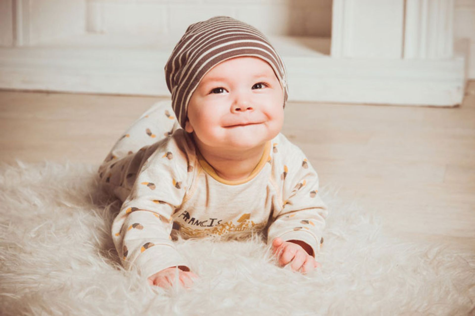 A young child in a cream dress on a cream-colored carpet