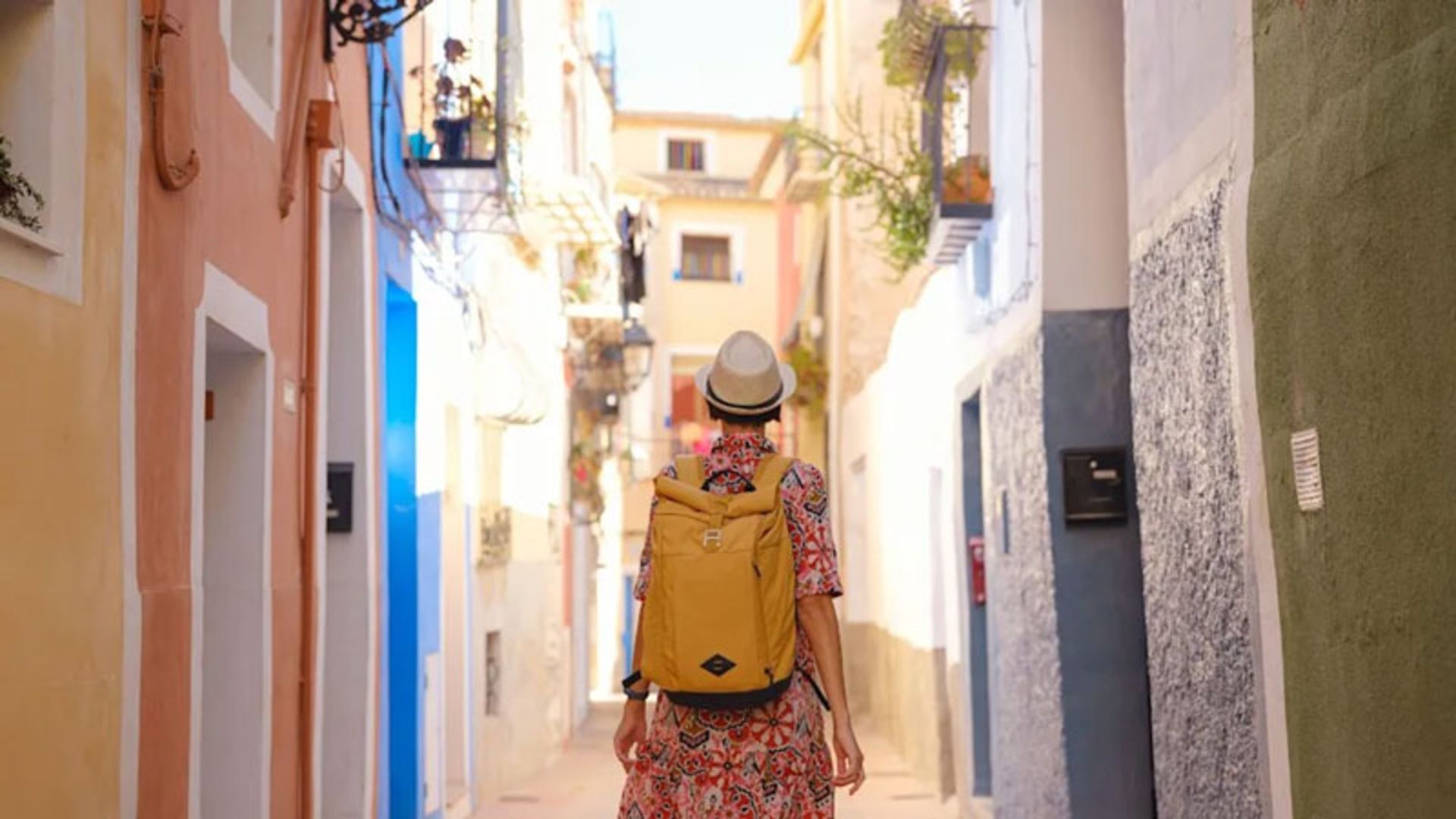 A person with a yellow backpack walking in a narrow and colorful alley