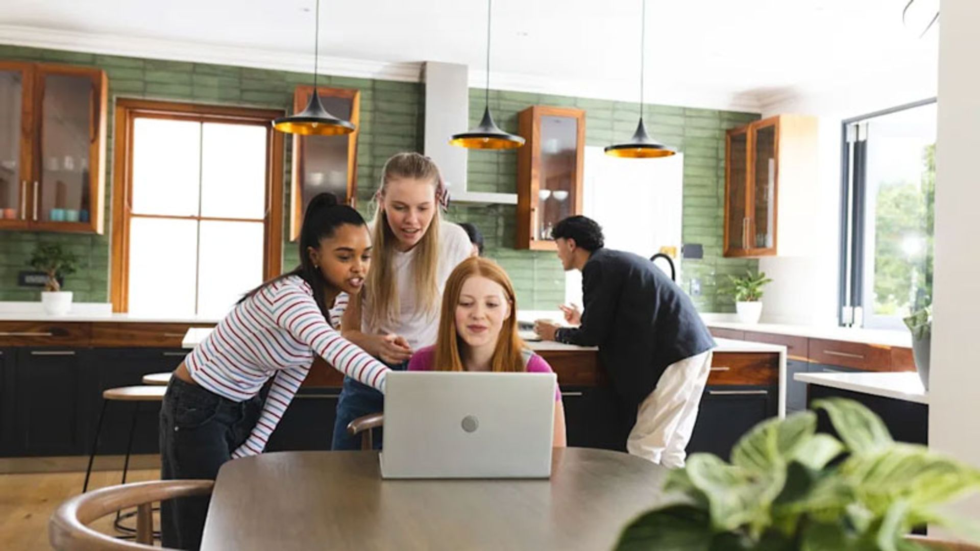 A group of young people around a laptop in a modern kitchen