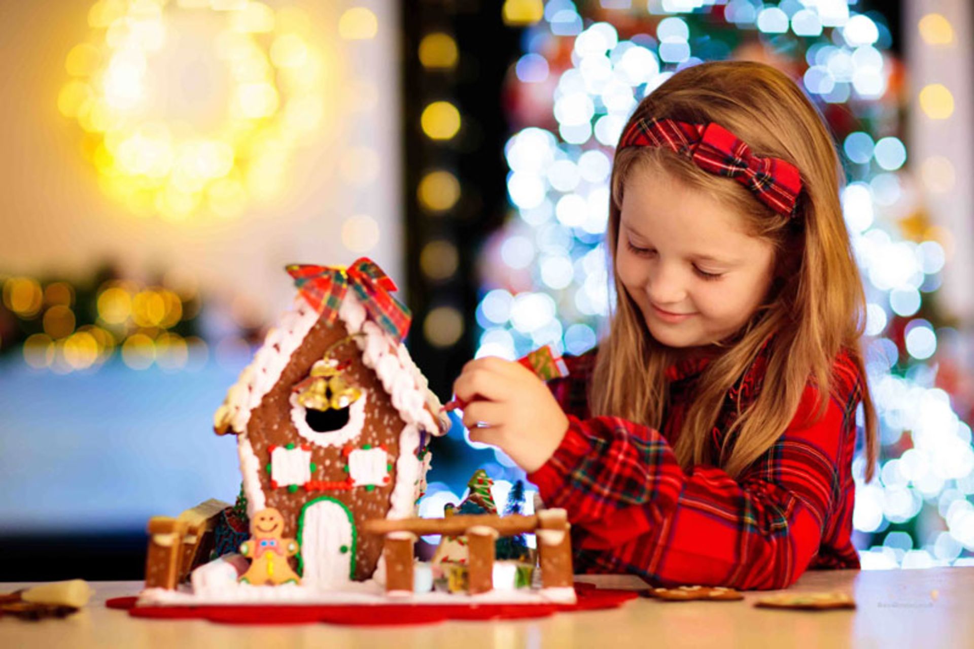 A child with a red plaid shirt and a gingerbread house