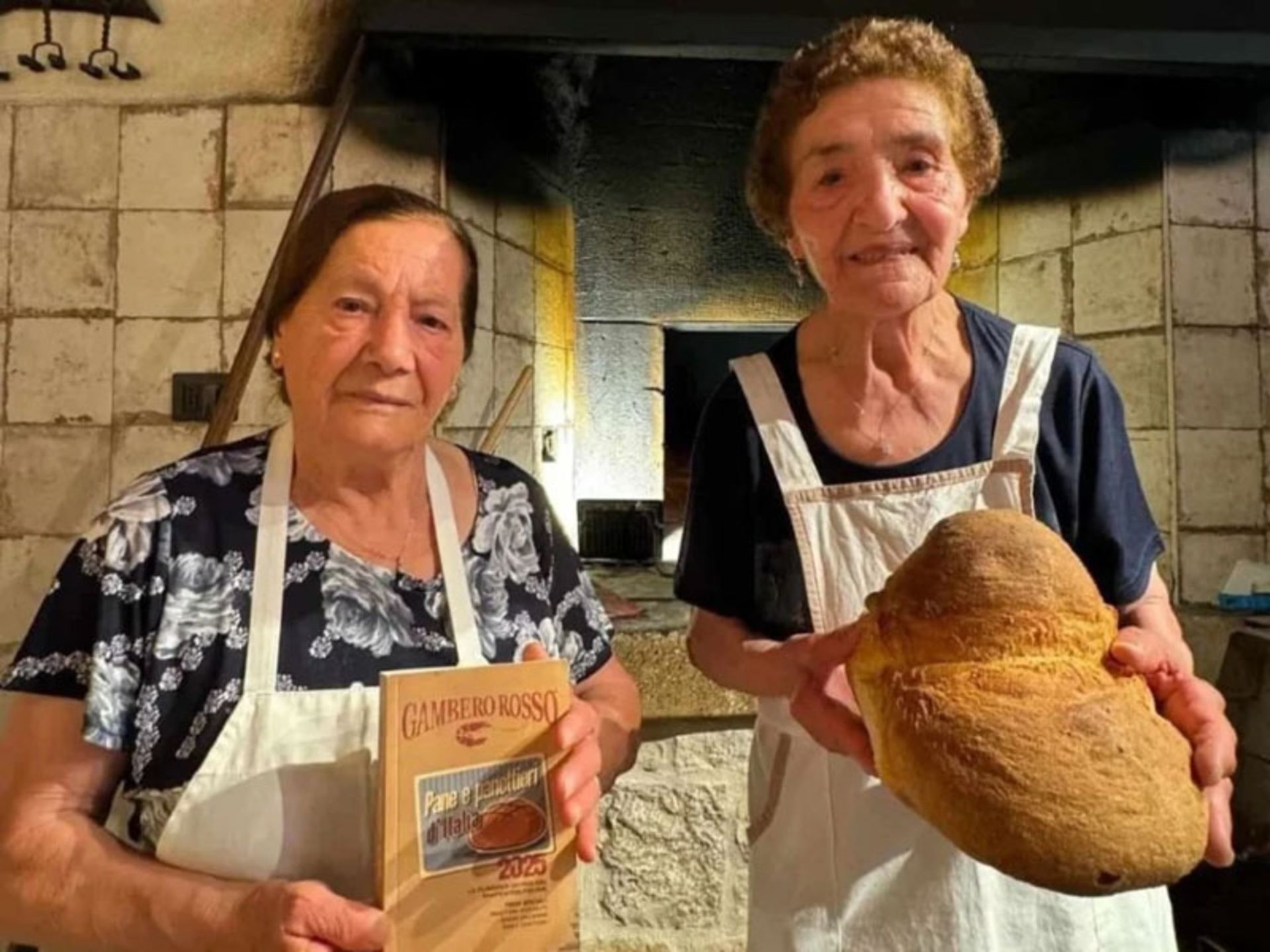 Two grandmothers in front of an ancient wood oven