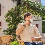 A man drinking coffee in an outdoor cafe with old architecture