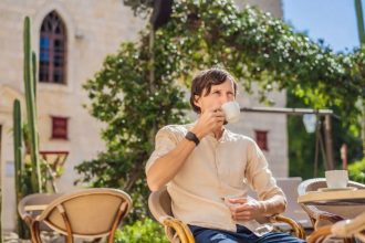 A man drinking coffee in an outdoor cafe with old architecture
