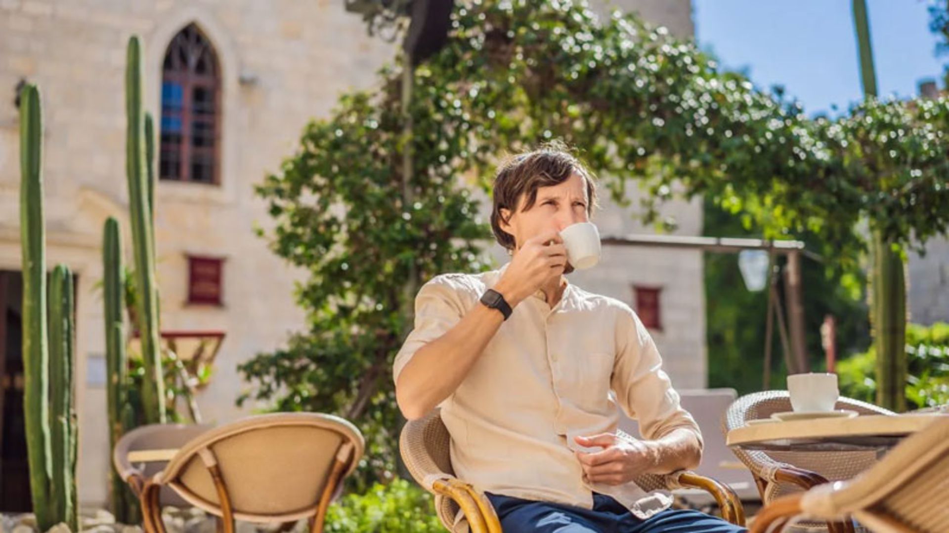 A man drinking coffee in an outdoor cafe with old architecture