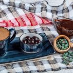A cup of coffee, a bowl of meningich dark dough, a wooden spoon with nuts and chocolate