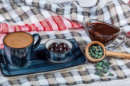 A cup of coffee, a bowl of meningich dark dough, a wooden spoon with nuts and chocolate