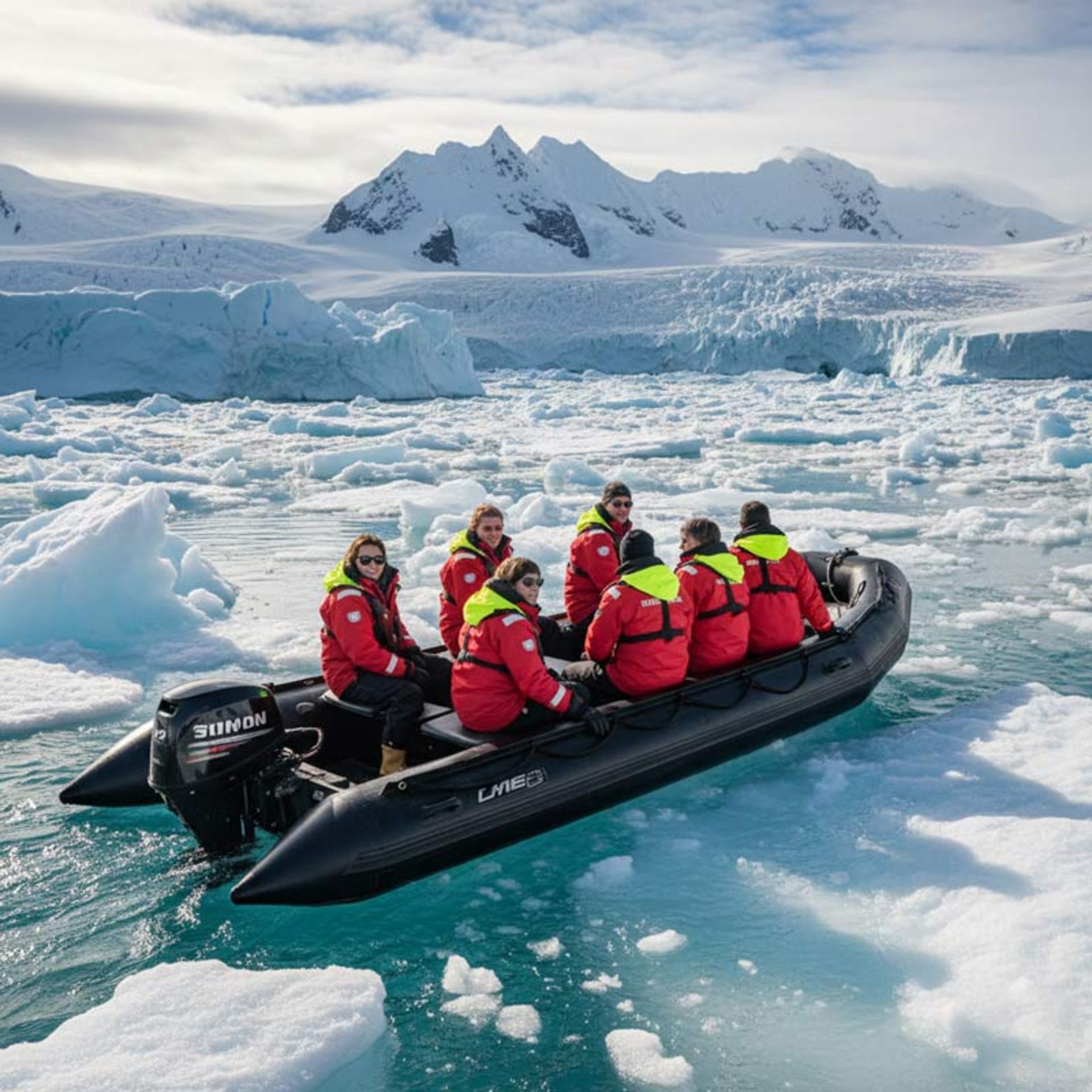 A Zodiac inflatable boat carrying passengers in red life jackets moving slowly through the floating ice
