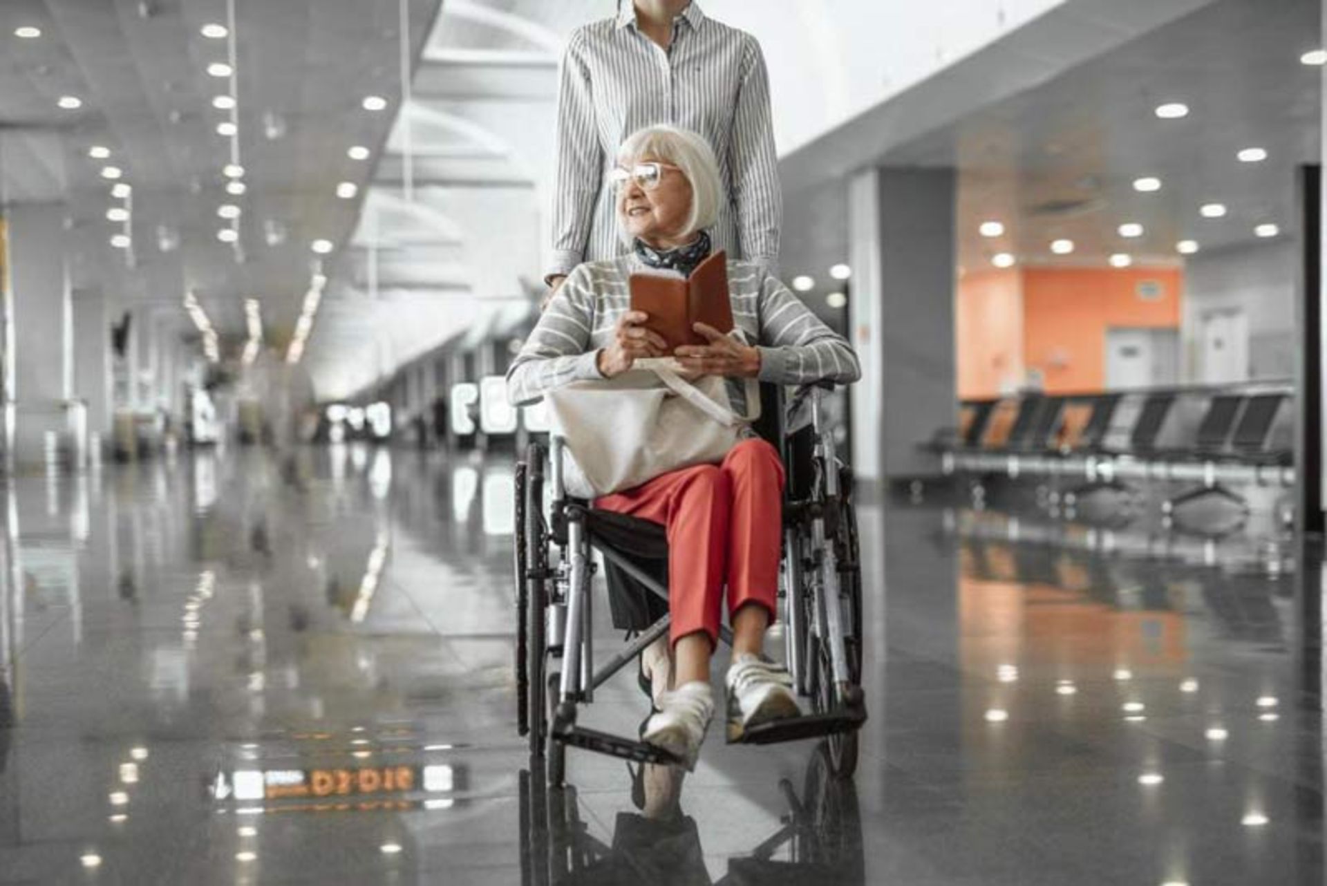 Elderly lady in wheelchair with travel documents in hand in modern terminal hall