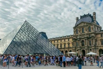 A close-up view of the glass pyramid of the Louvre Museum in Paris on a partly cloudy day
