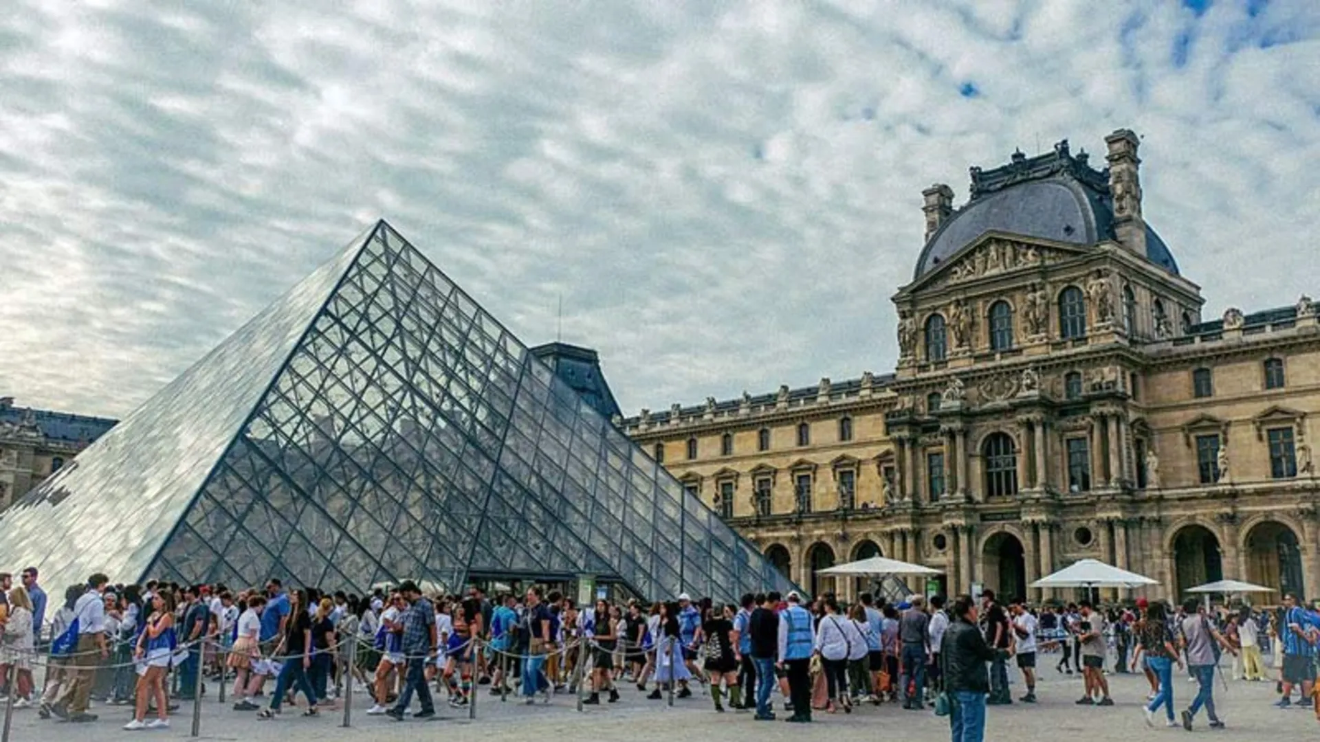 A close-up view of the glass pyramid of the Louvre Museum in Paris on a partly cloudy day