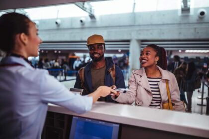 The smile of the airport attendant while handing over the documents and flight card to the passenger couple behind the counter